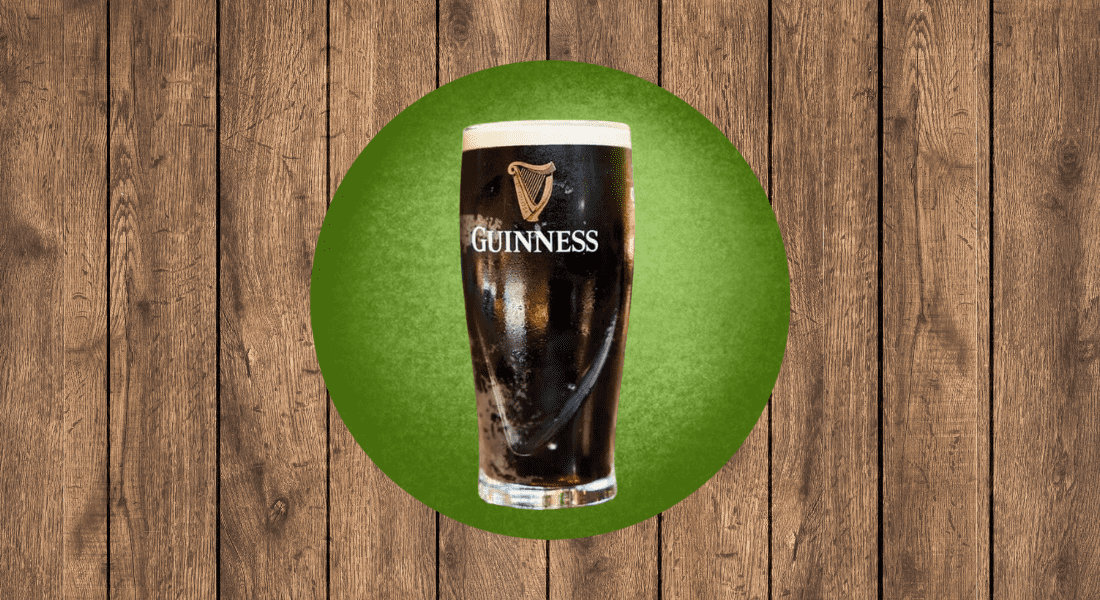 A pint of dark beer with a frothy top, labeled "Guinness," is centered on a green circle over a wooden background.